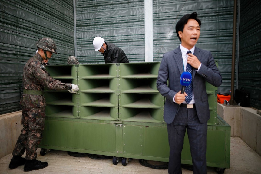A reporter prepares a news report as South Korean soldiers dismantle loudspeakers.