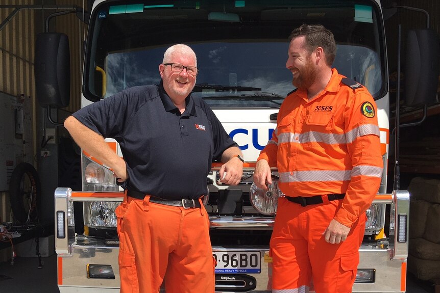 Two men in orange overalls in front of an SES truck.