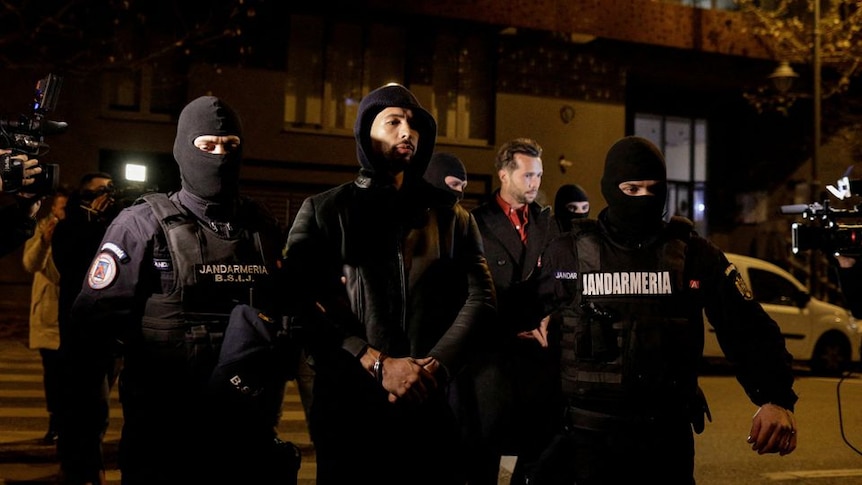 Andrew Tate and Tristan Tate are escorted by police officers outside the headquarters  at night