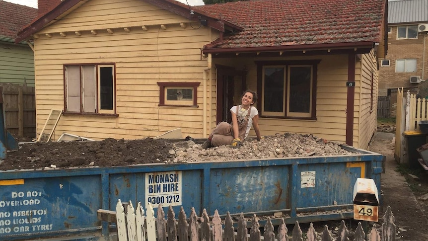 A young woman sitting on a pile of rubble in a skip bin