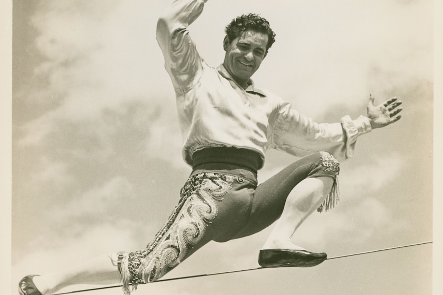 A black and white photo of a man with black hair in a Spanish costume on a highwire.