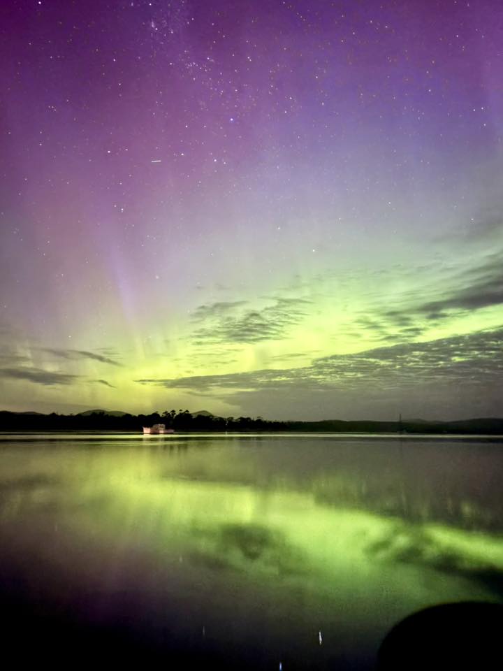 Luces verdes, amarillas, rosadas y violetas en el cielo reflejadas en el agua debajo.