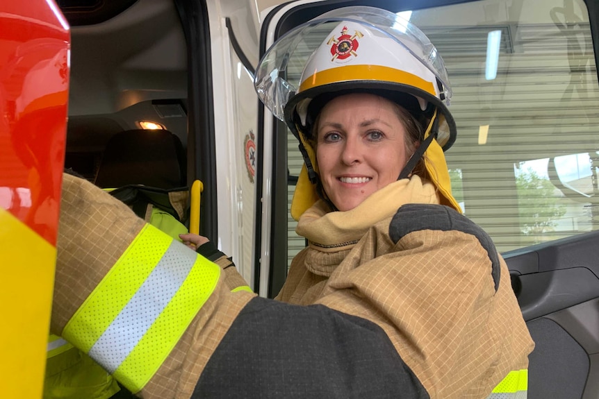 Close-up photo of woman in firefighter uniform getting into truck and smiling.