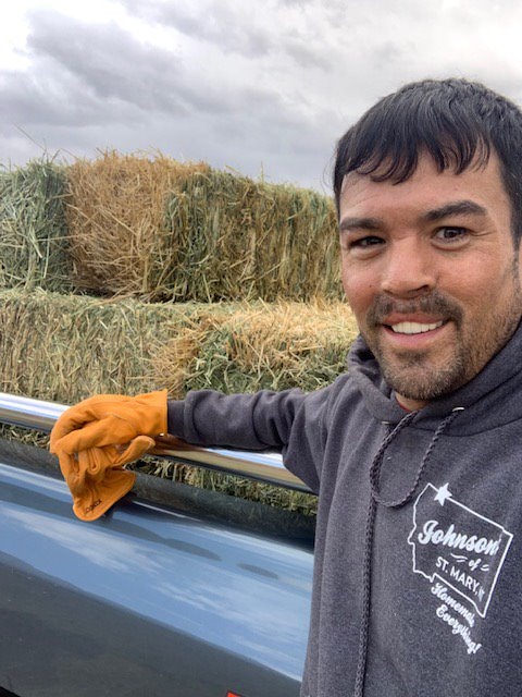 Man smiling with hay stacks in the background.