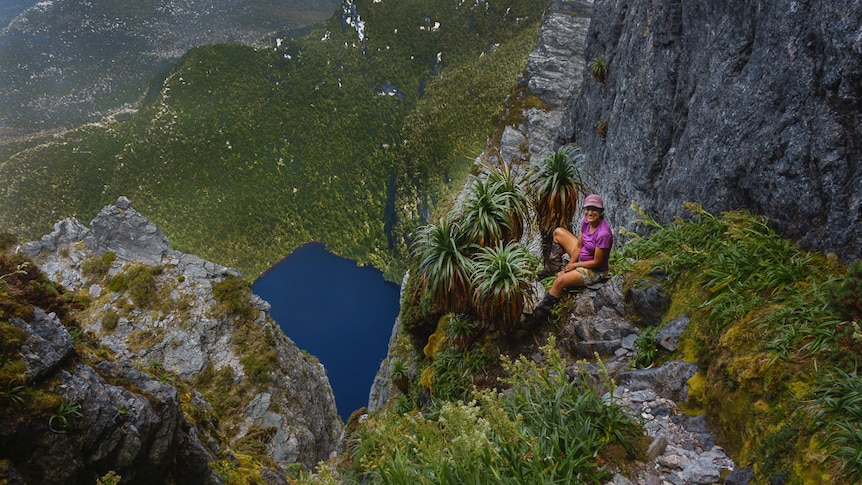A woman on the side of a mountain cliff, with a lake way below