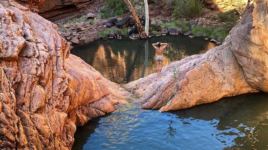 waterhole surrounded by red cliffs and swimmer in foreground.