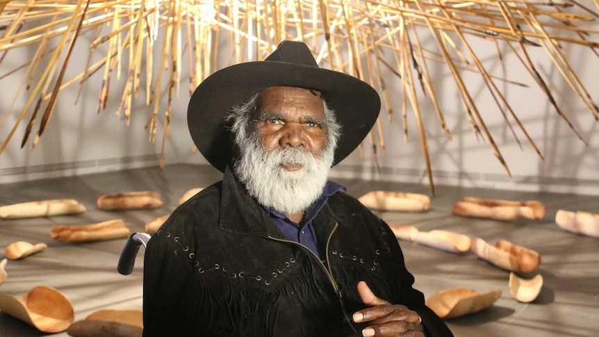 Aboriginal artist Mike Williams sits in front of an installation.