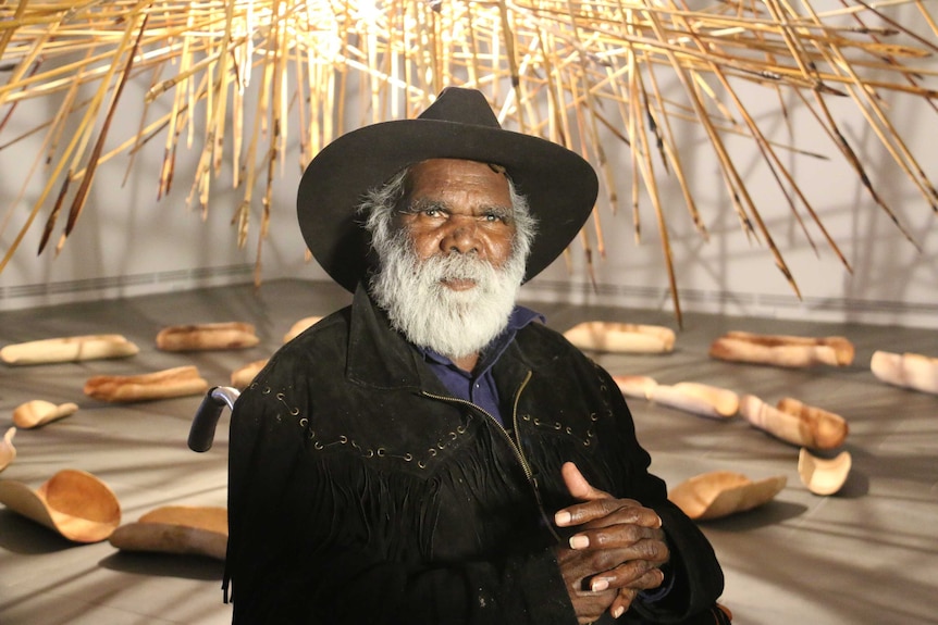 Aboriginal artist Mike Williams sits in front of an installation.