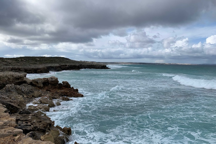 A rocky coastline is battered by waves on an overcast day.