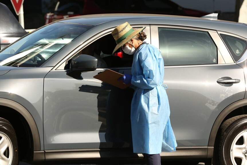 A woman in scrubs looks at a clipboard near a car
