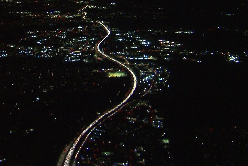 A bright stream of car headlights stuck in traffic on the highway. A photo taken from a helicopter. 