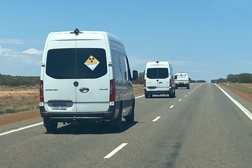 Two white vans and a white ute drive into the distance on a highway in regional WA.