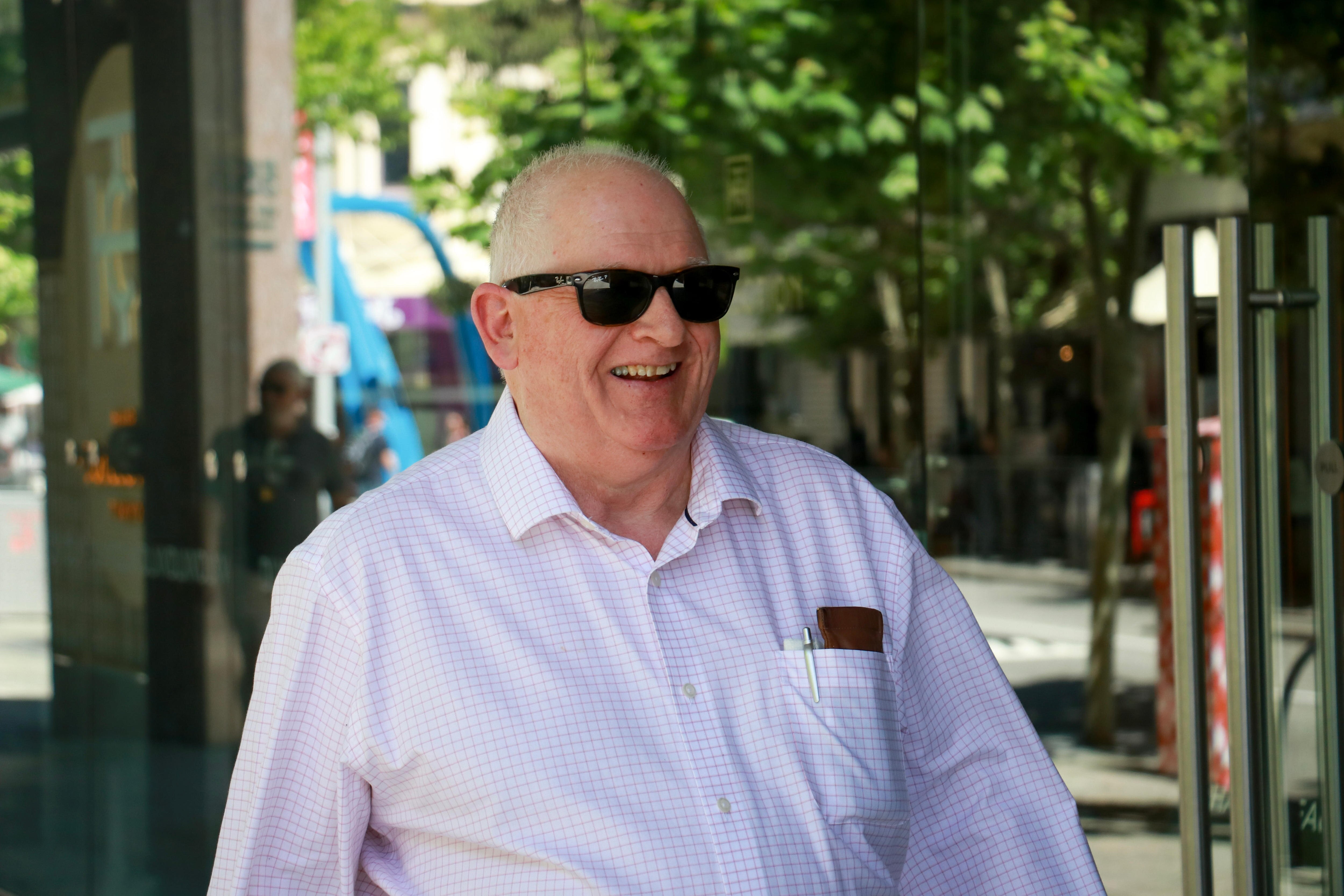 Um homem mais velho, de cabelos brancos, passa pela câmera. 