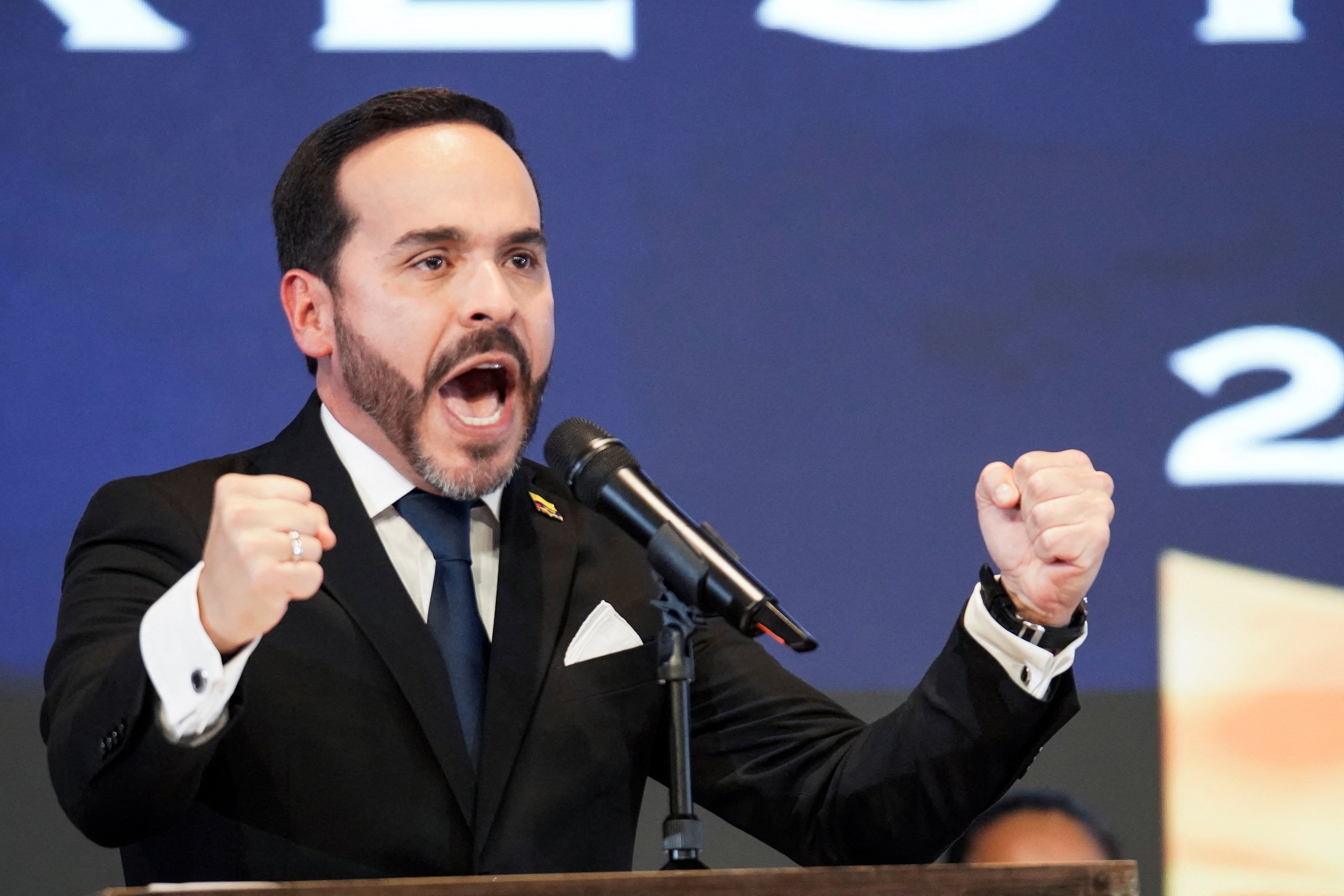 Abelardo de la Espriella mid-speech with two fists raised and his mouth open in front of a microphone.