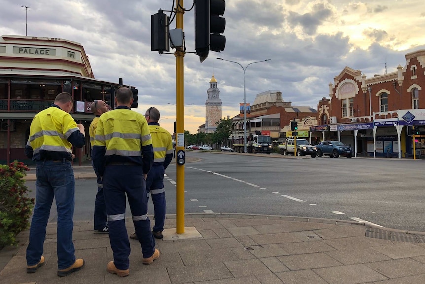 Four men in high vis outfits wait to cross the road.