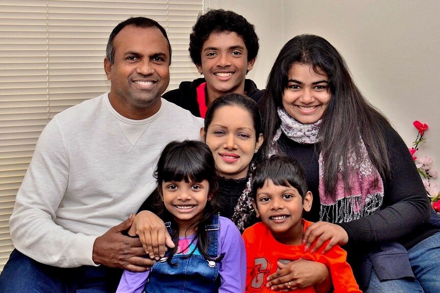A family of two parents and four children smile at the camera.