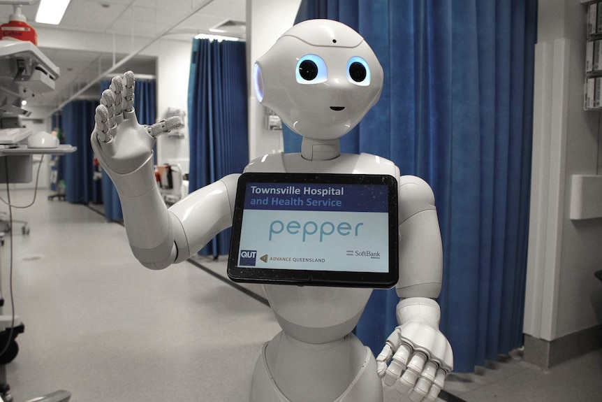 A robot standing inside a hospital ward waves its hand at the camera.