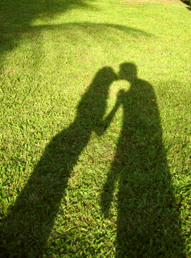 Shadow of couple kissing on green grass backdrop