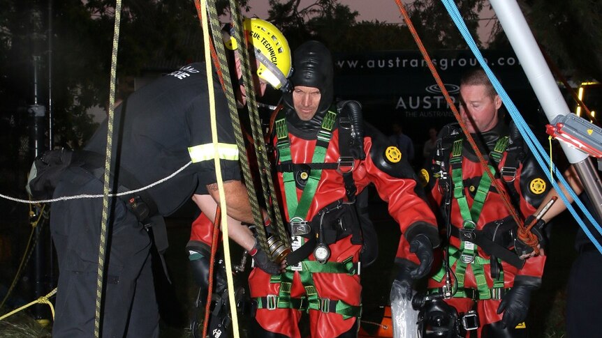 Police divers prepare to be lowered into a sewer to retrieve a body.