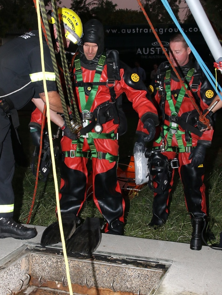Police divers prepare to be lowered into a sewer to retrieve a body.