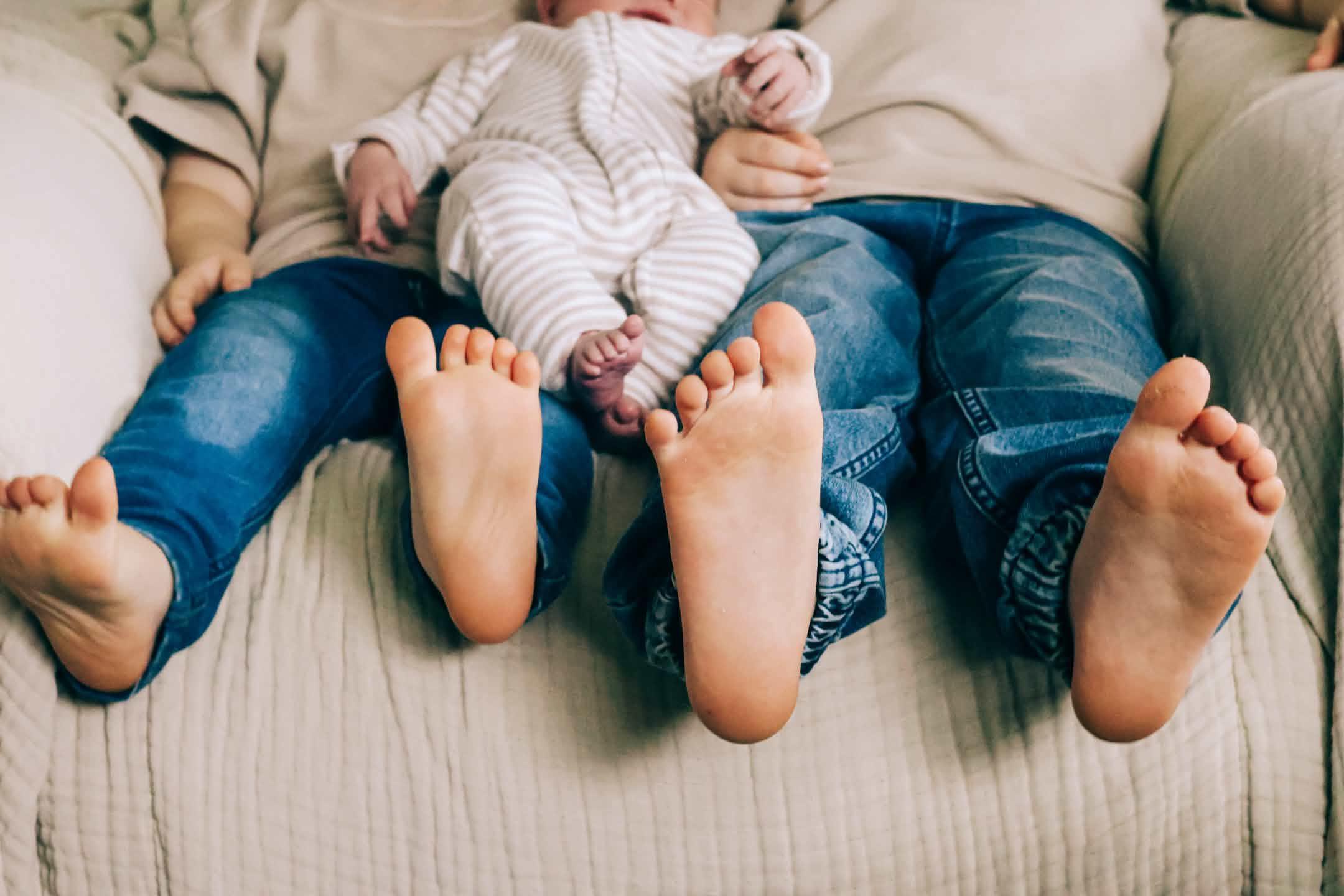 The feet of three children as they sit together on a sofa.