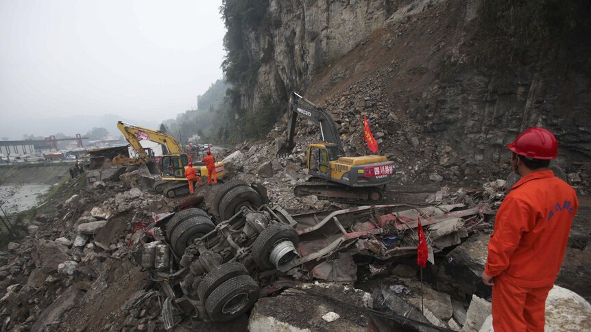 A rescuer looks on as excavators clean up a road which is blocked by a landslide after China's earthquake.