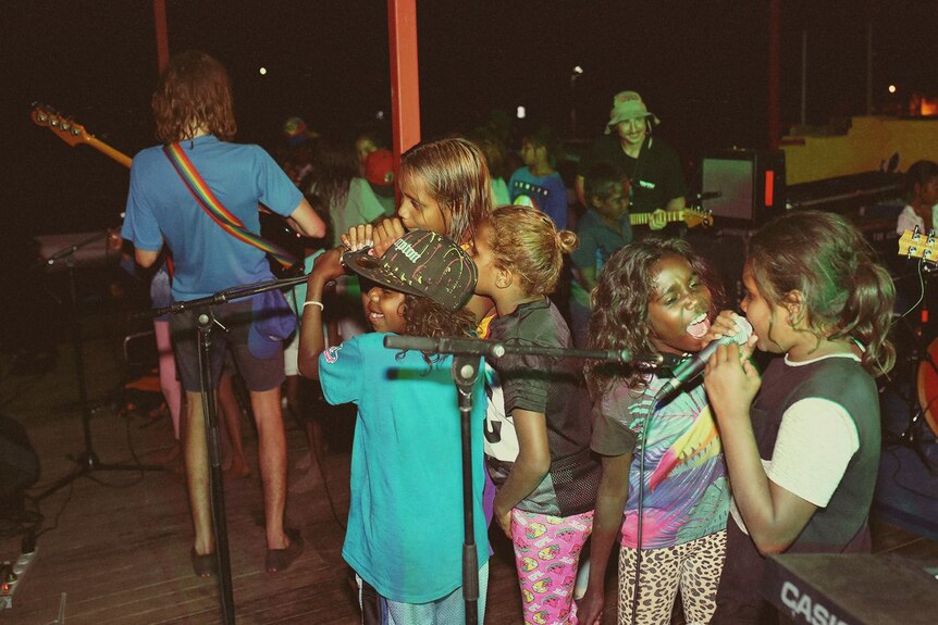 Kids sing into microphones at a night-time gig.
