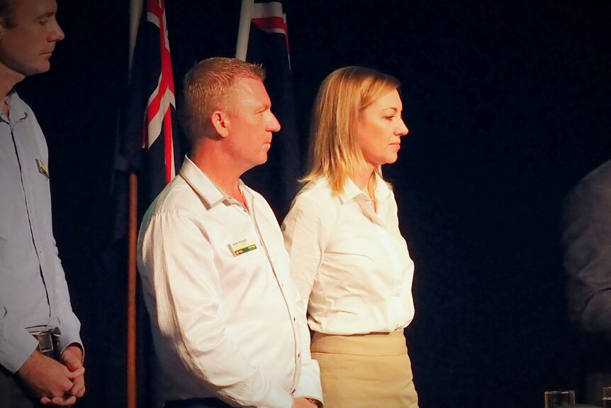 A man and woman wearing white shirts stand on a function stage