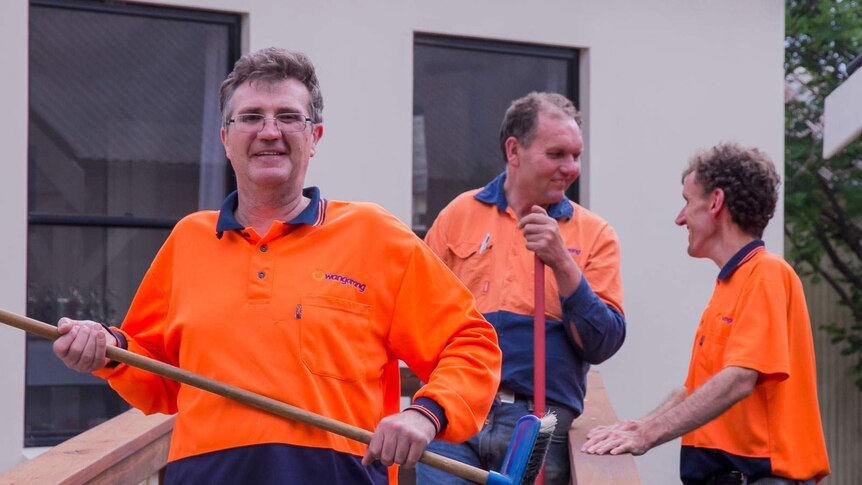 A man holding broom with two others also in high visibility gear standing outside a house
