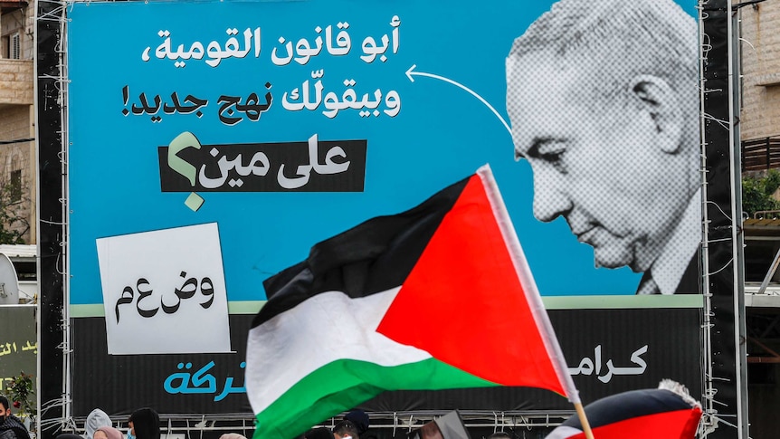 A Palestinian flag is waved in front of an electoral billboard of Israeli prime Minister Benjamin Netanyahu.