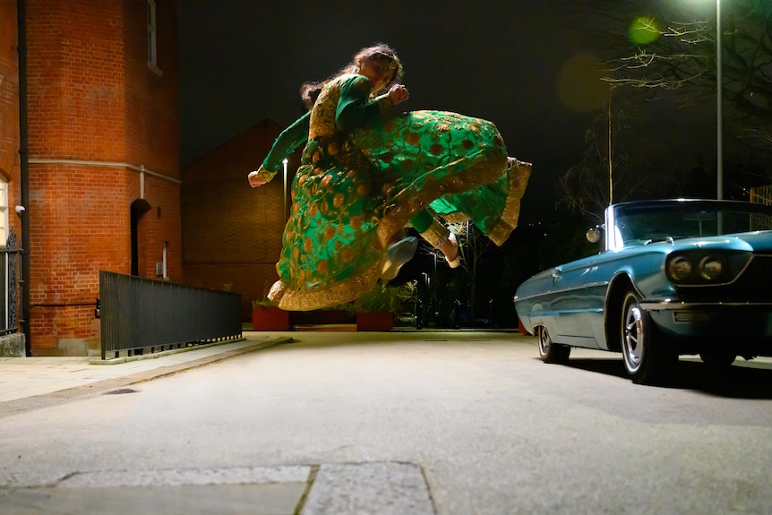 Priya Kansara, a young Pakistani women in a green sari in mid-air on a street, performing a martial arts move.