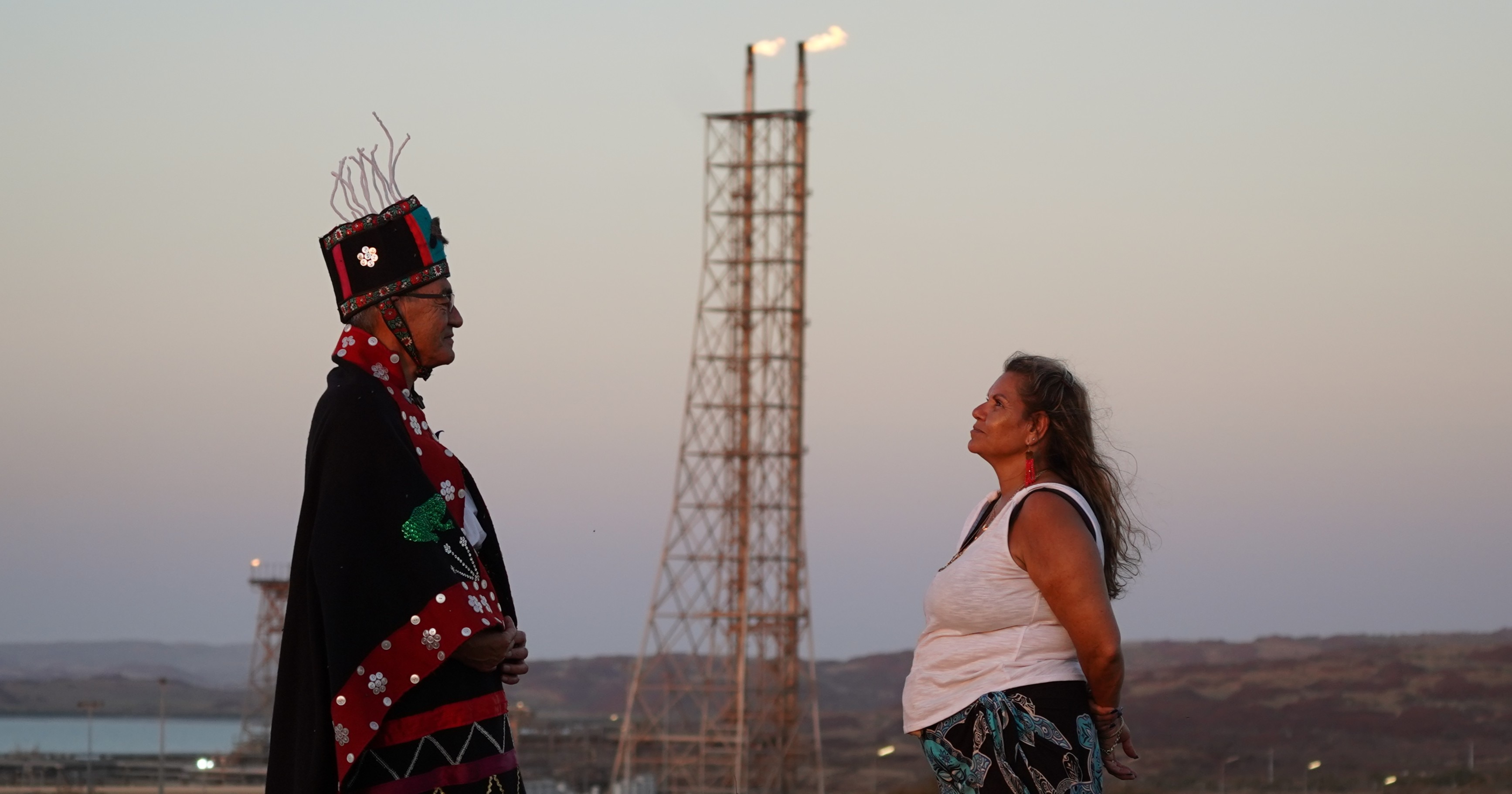 Un hombre con vestimenta tradicional se encuentra frente a una mujer de piel oscura que lleva una camiseta blanca.