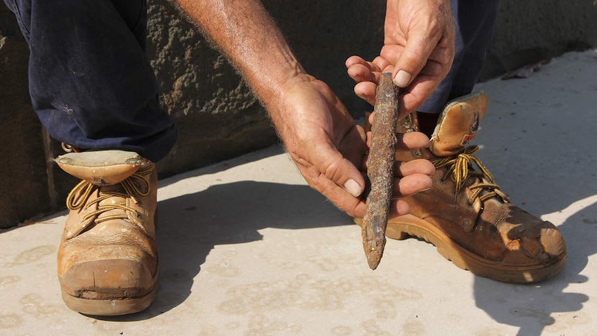 A photo of a rusted chisel being held in the hands of Clayton Dwyer.