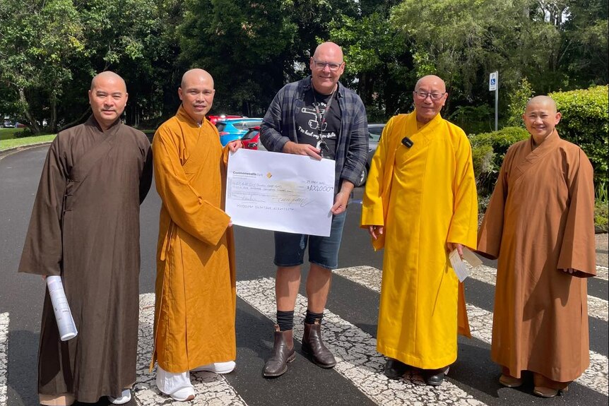 Mayor holding a large cheque standing next to four monks wearing long yellow and brown robes