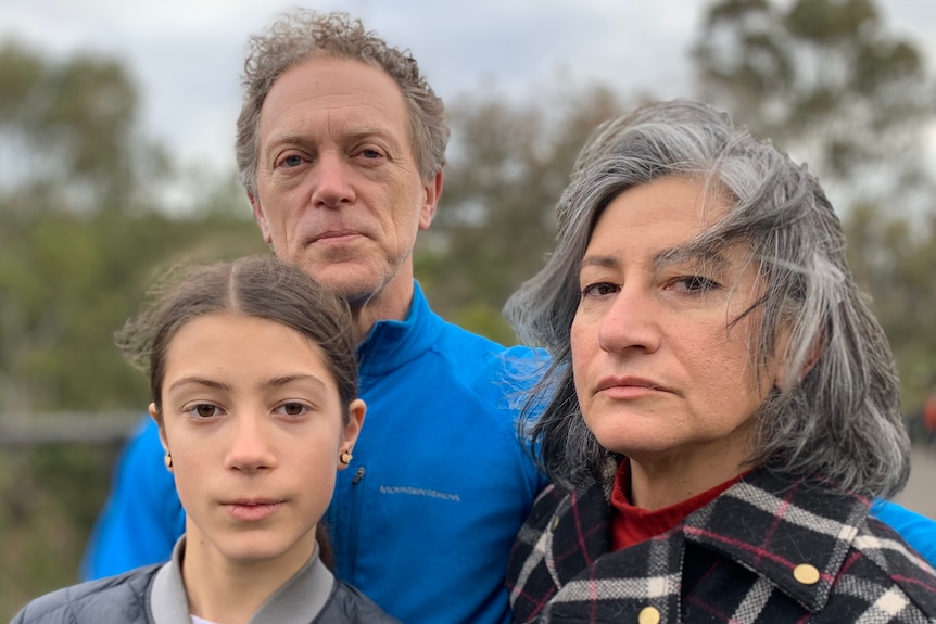 A woman wearing a checked coat with a man and a young girl beside her.