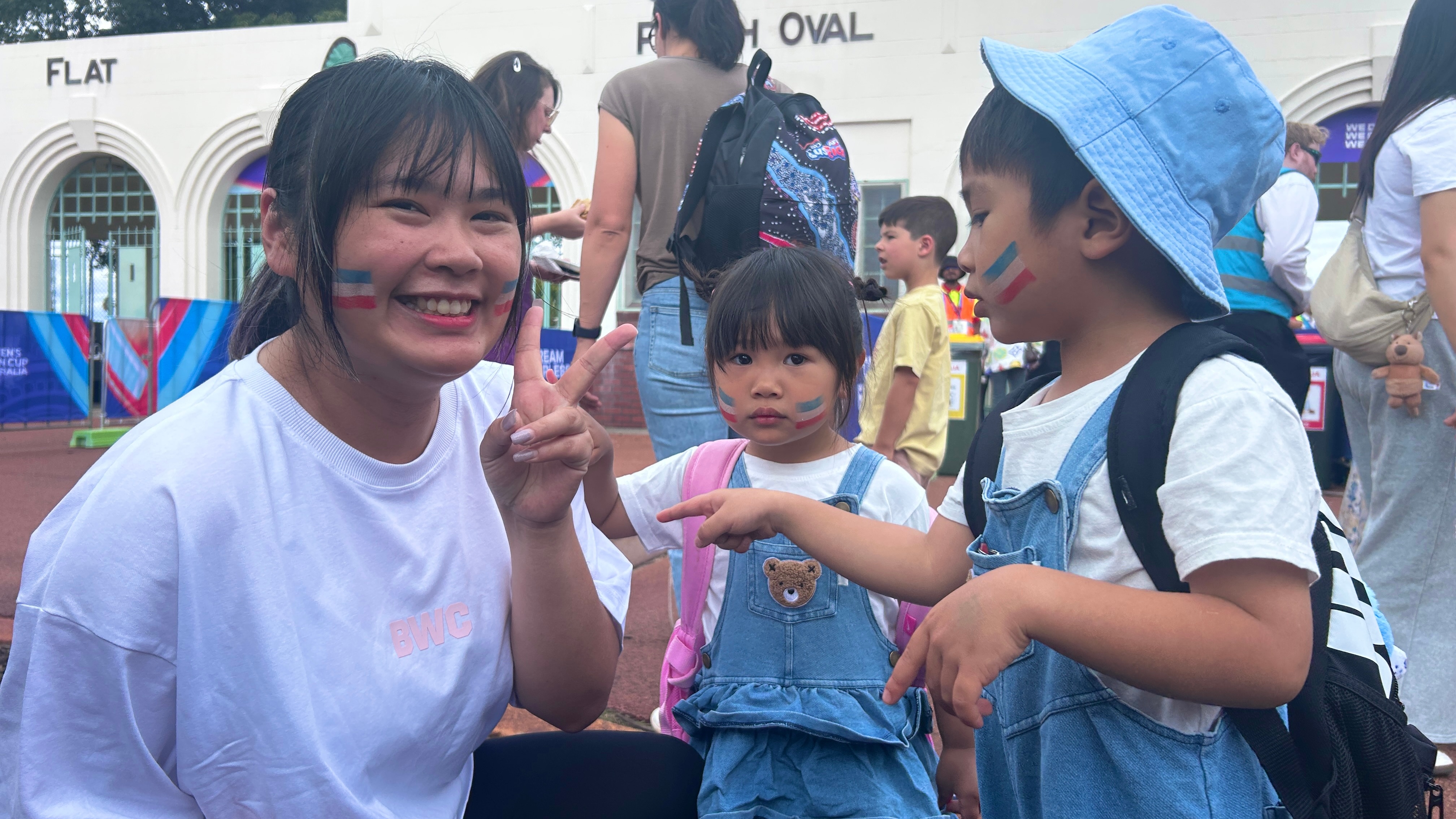 Uma mulher com pintura facial azul faz uma "sinal de paz" com duas crianças ao lado dela