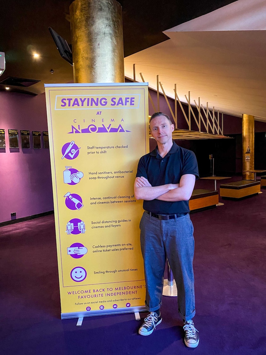 Kristian Connelly stands next to signage in the cinema that directs patrons on COVID-19 precautions.