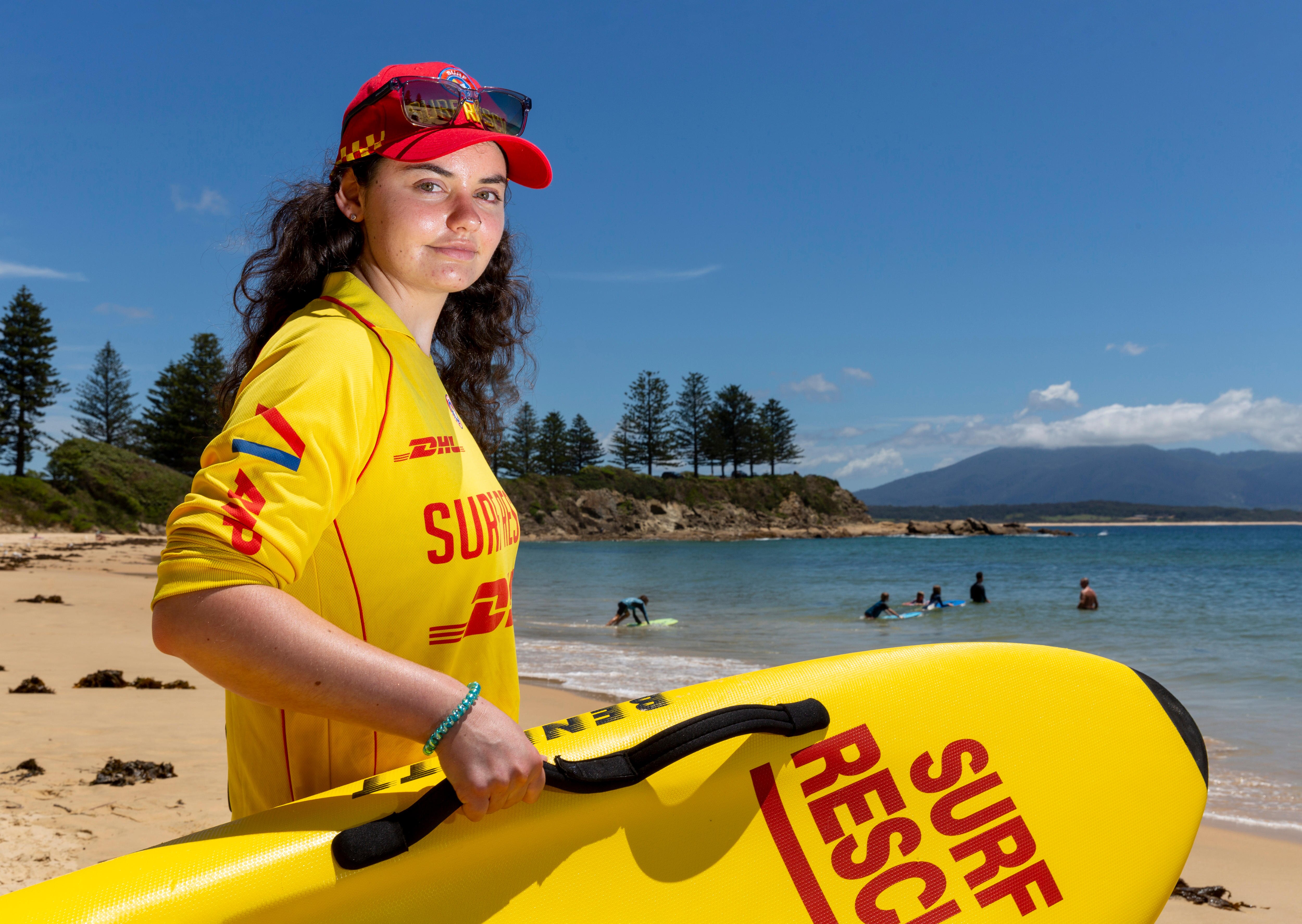 A young woman in surf life saving uniform on the a sunny beach while holding a club board 