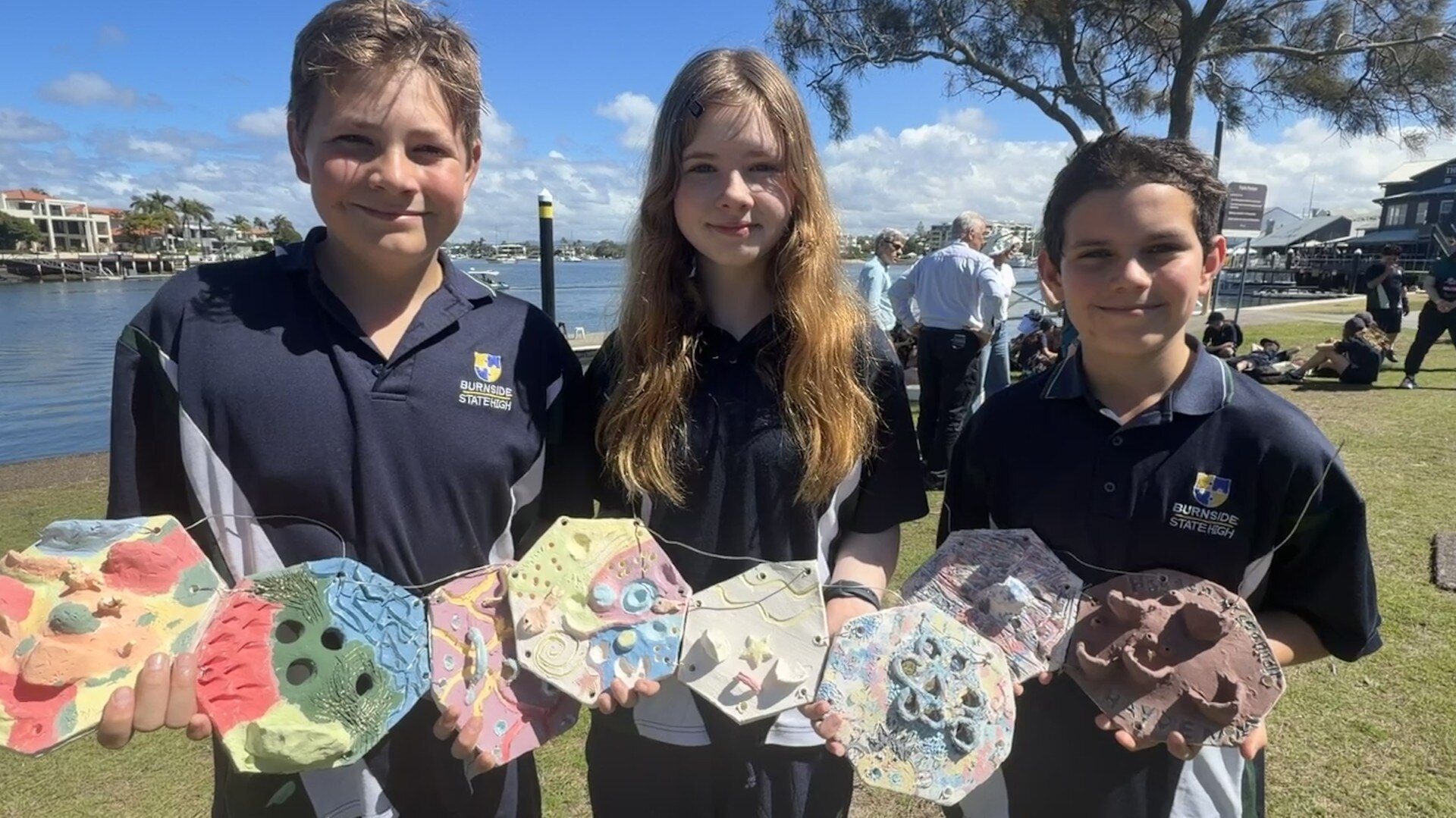 Three students hold their colourful tiles up and smile.