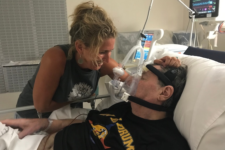 A woman touches the head of a man who is in a hospital bed