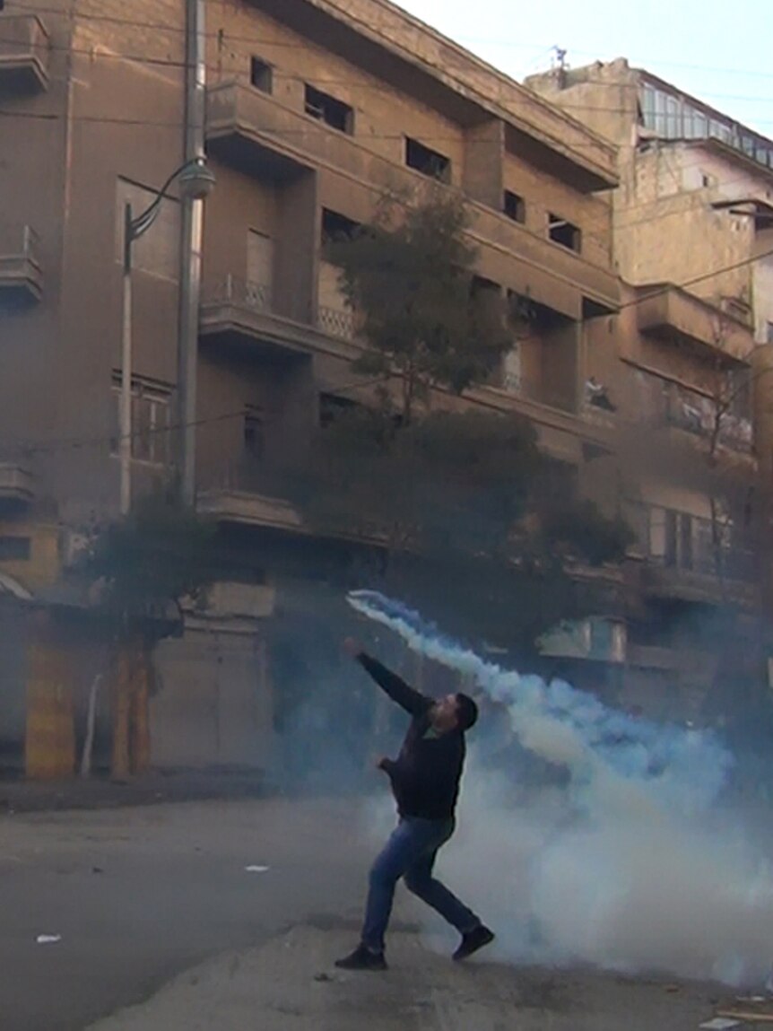 A protester throws a tear gas bomb in Homs