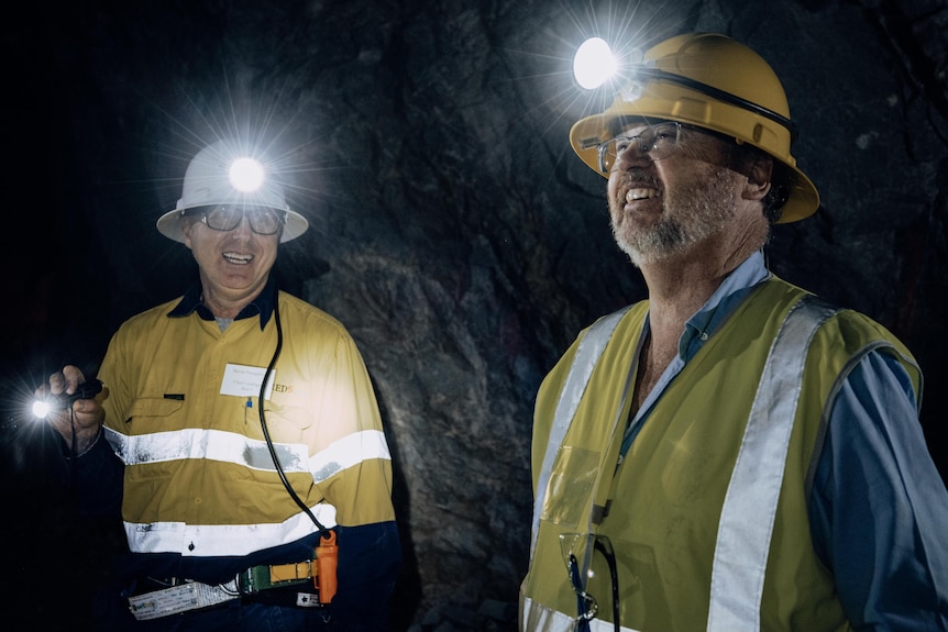 Two men wearing hard hats with lamps on in a dark underground mine.  