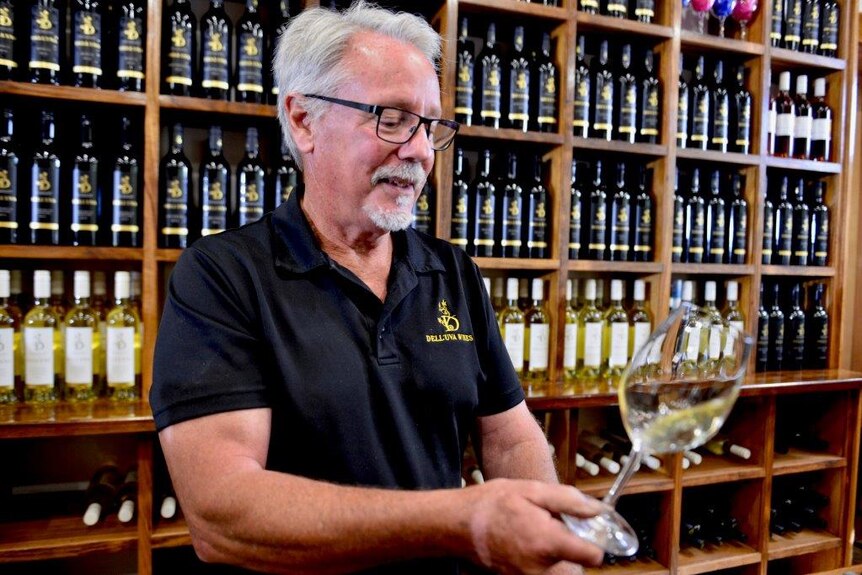 A man holds a wine glass in front of shelves filled with bottles.