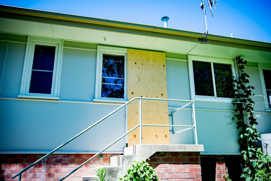 A wooden board covers a back door on a blue home.