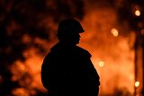 A firefighter in silhouette, a large fire raging behind him.