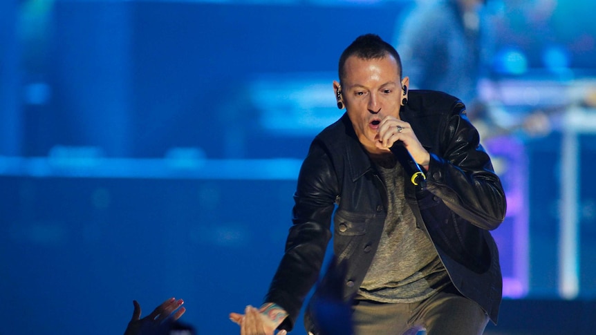 Singer leans over to sing with crowd at rock concert.