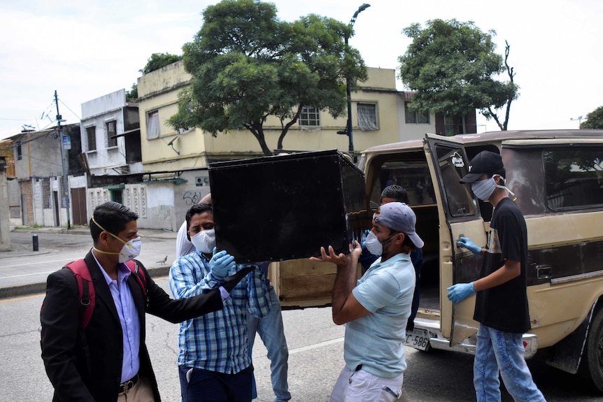 Men in face masks hoist a coffin out of a truck in Ecuador