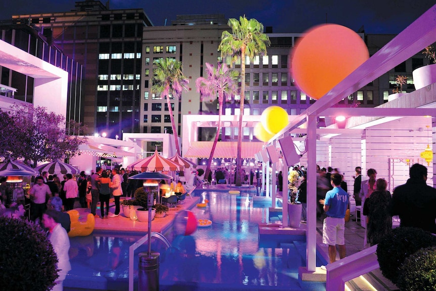 People stand around a swimming pool at night