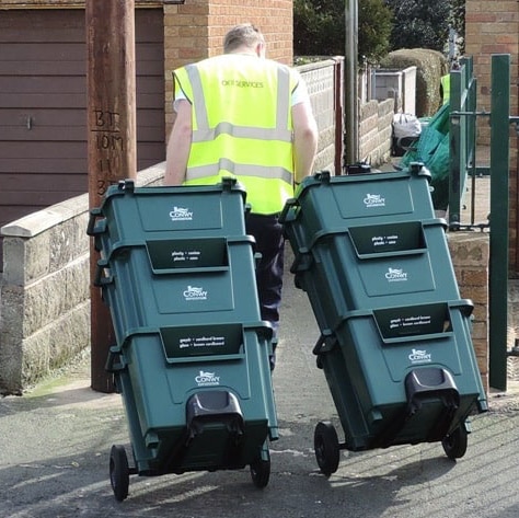 A rubbish worker dragging recycling crates on a wheeled trolley.