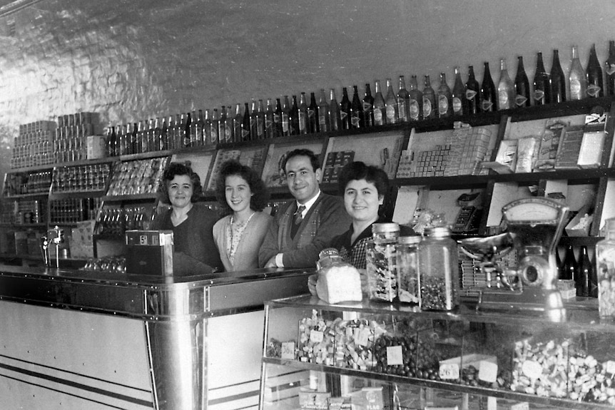A black and white photo of a Lebanese family standing behind the counter of a cake and sweets shop.